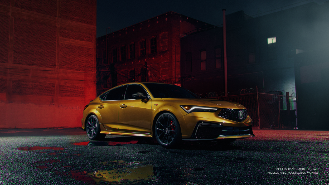 3/4 front view of gold Integra Type S at night, parked in an urban alley parking lot in front of a wall lit with red lighting.